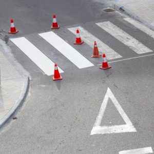 Road painting maintenance concept. Painting white street lines on pedestrian crossing and road cones on city. No people